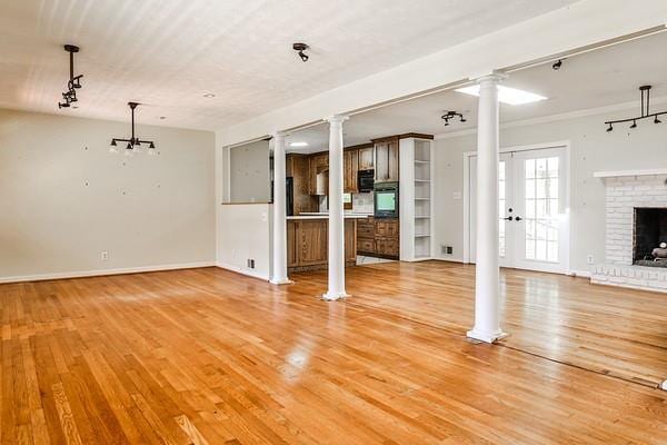 unfurnished living room featuring a brick fireplace, baseboards, decorative columns, and light wood finished floors