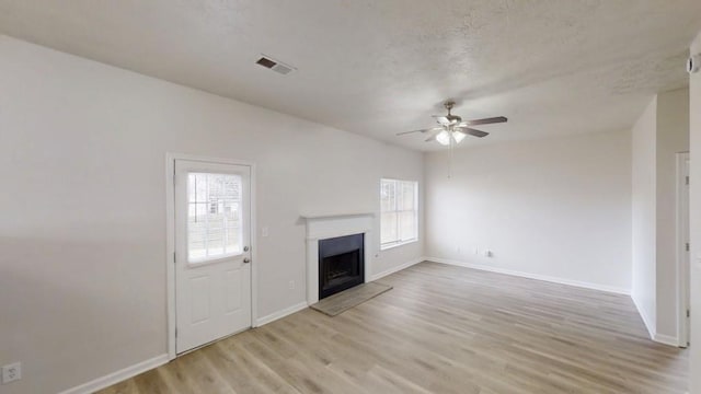 unfurnished living room with a ceiling fan, visible vents, baseboards, light wood-style flooring, and a fireplace with raised hearth