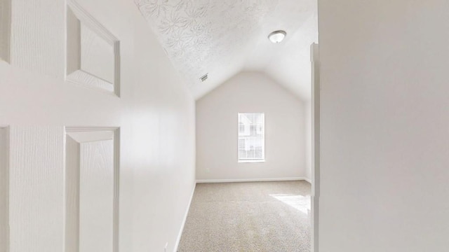 additional living space featuring visible vents, baseboards, lofted ceiling, carpet flooring, and a textured ceiling