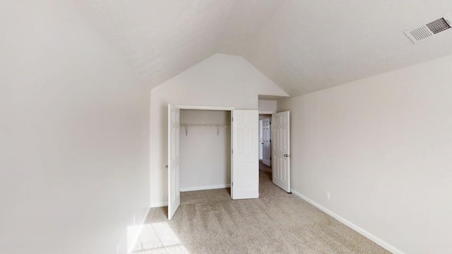 unfurnished bedroom featuring visible vents, baseboards, light colored carpet, vaulted ceiling, and a closet