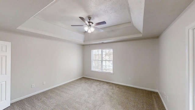 spare room with a tray ceiling, baseboards, carpet, and a ceiling fan