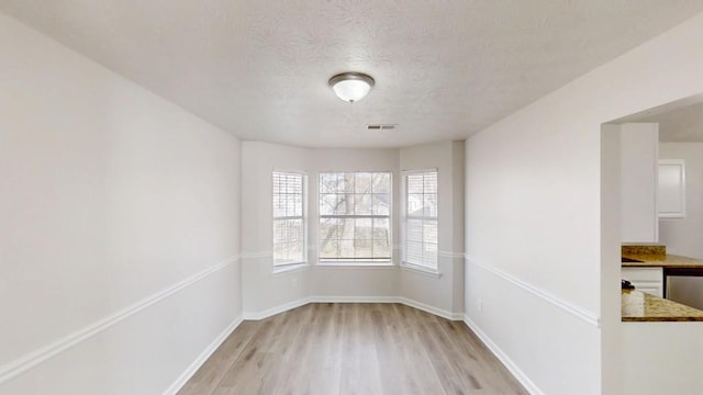 spare room with light wood-type flooring, visible vents, baseboards, and a textured ceiling