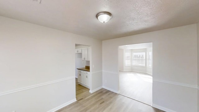 spare room with light wood-type flooring, baseboards, and a textured ceiling