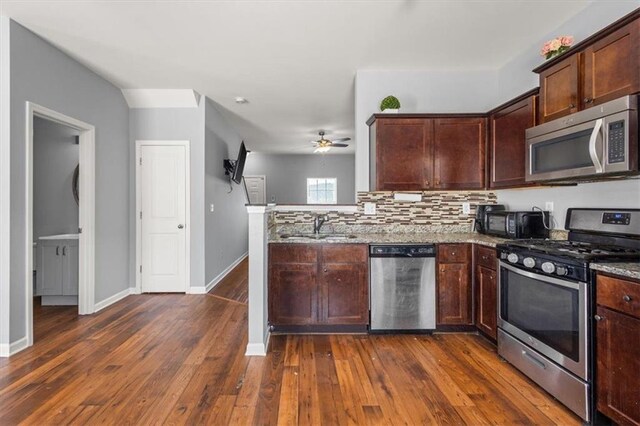 kitchen with dark wood-style flooring, a peninsula, ceiling fan, stainless steel appliances, and a sink