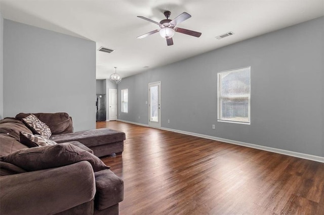 living area featuring ceiling fan with notable chandelier, visible vents, baseboards, and dark wood-style flooring