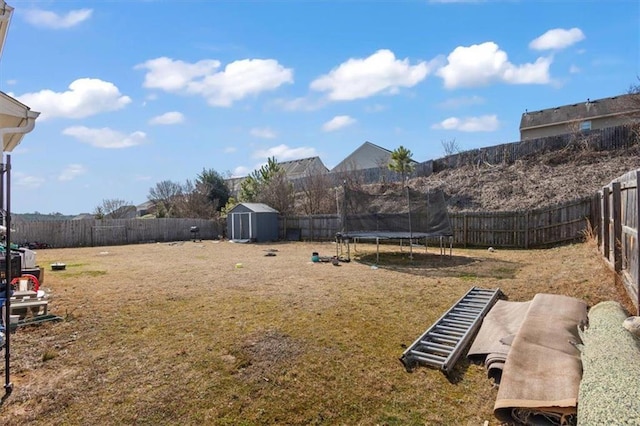 view of yard with a trampoline, an outdoor structure, a fenced backyard, and a shed