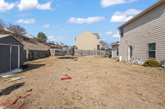 view of yard with a trampoline, a fenced backyard, an outbuilding, and a shed