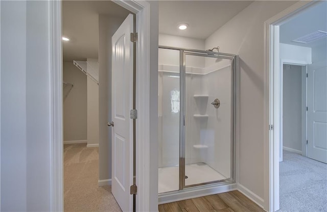 bathroom with a walk in closet, visible vents, a shower stall, and baseboards