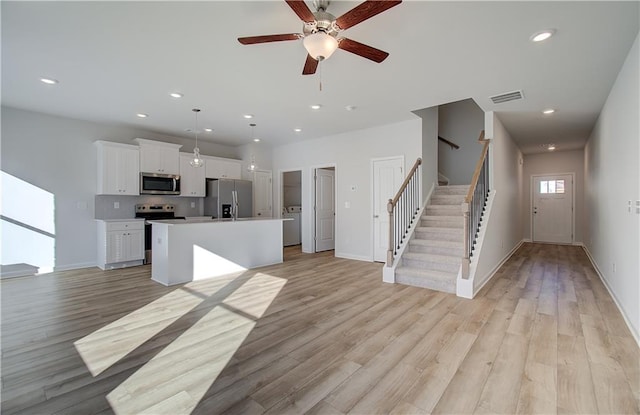 kitchen featuring an island with sink, white cabinets, stainless steel appliances, and open floor plan