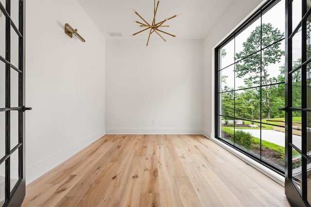 empty room with french doors, light hardwood / wood-style floors, and an inviting chandelier