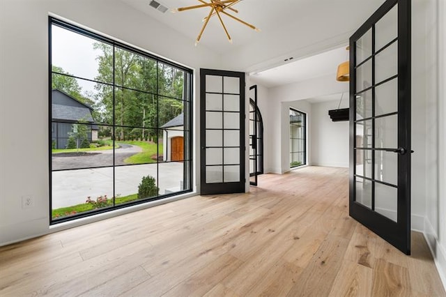 empty room with french doors, a notable chandelier, and light hardwood / wood-style flooring