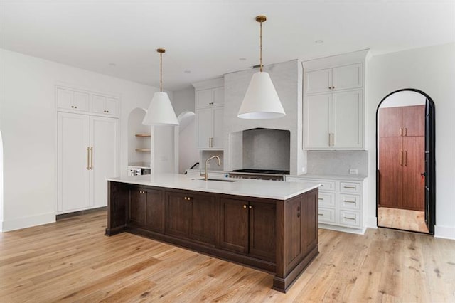 kitchen featuring white cabinetry, sink, hanging light fixtures, light hardwood / wood-style flooring, and a center island with sink