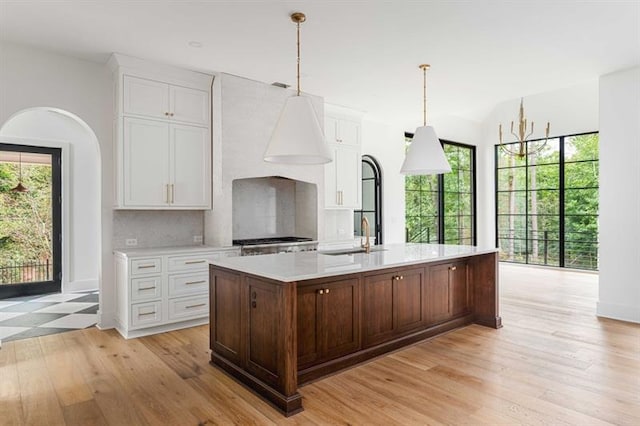 kitchen featuring backsplash, decorative light fixtures, a kitchen island with sink, and sink