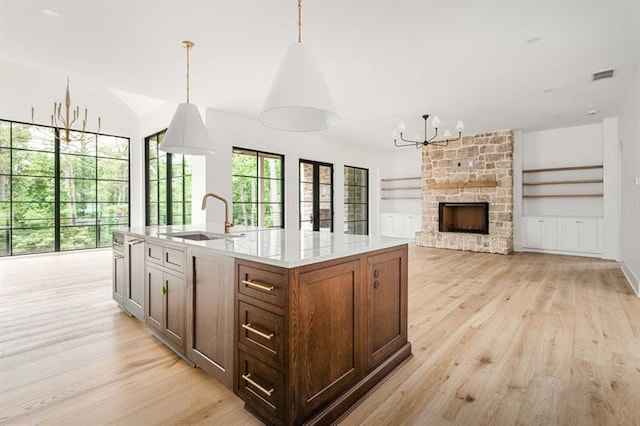 kitchen with a stone fireplace, sink, an island with sink, decorative light fixtures, and light hardwood / wood-style floors