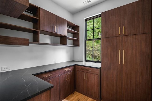 kitchen with dark brown cabinets, light hardwood / wood-style floors, and dark stone countertops