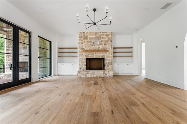 unfurnished living room with built in shelves, french doors, a stone fireplace, light hardwood / wood-style flooring, and a chandelier