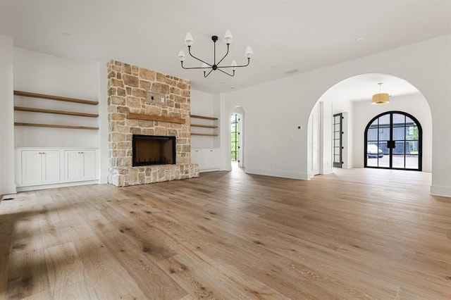 unfurnished living room featuring light hardwood / wood-style floors, a stone fireplace, and an inviting chandelier