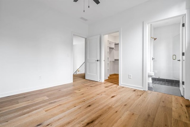 unfurnished bedroom with ensuite bathroom, ceiling fan, a spacious closet, and light wood-type flooring