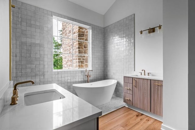 bathroom featuring wood-type flooring, vaulted ceiling, a bathtub, vanity, and tile walls