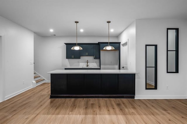 kitchen with sink, a center island, hanging light fixtures, and light hardwood / wood-style flooring