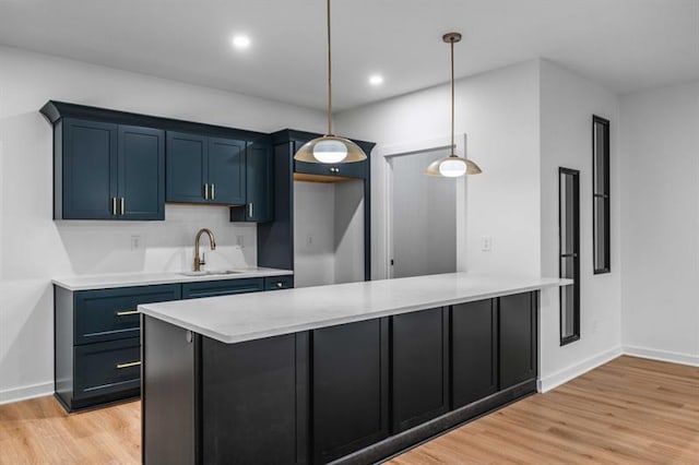 kitchen featuring blue cabinetry, sink, hanging light fixtures, and light hardwood / wood-style flooring