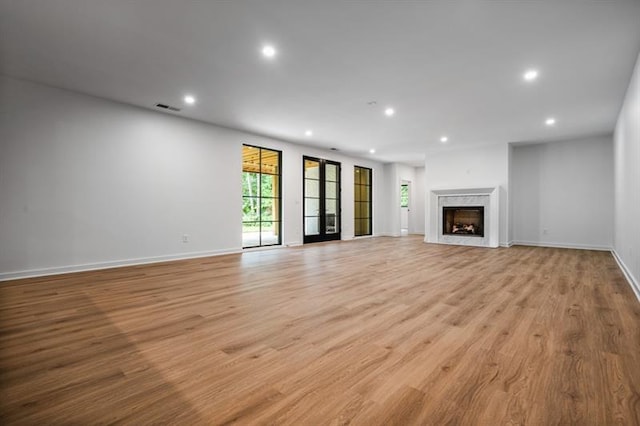 unfurnished living room featuring light wood-type flooring, a fireplace, and french doors