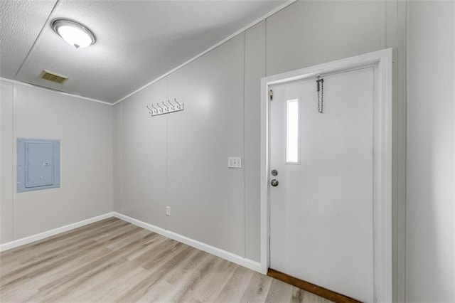 foyer with lofted ceiling, crown molding, electric panel, a textured ceiling, and light hardwood / wood-style floors