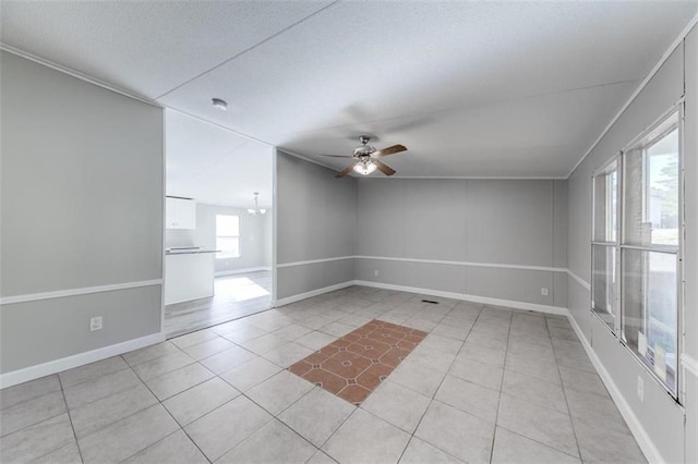 tiled empty room featuring ceiling fan with notable chandelier and a wealth of natural light