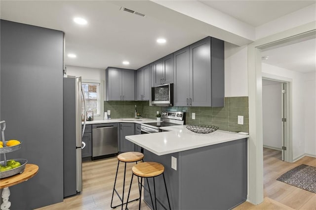 kitchen featuring gray cabinetry, a breakfast bar area, stainless steel appliances, and kitchen peninsula