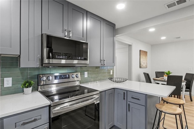 kitchen with gray cabinets, stainless steel appliances, a breakfast bar, and kitchen peninsula