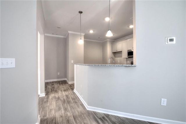 kitchen featuring pendant lighting, dark wood-type flooring, kitchen peninsula, light stone counters, and white cabinetry