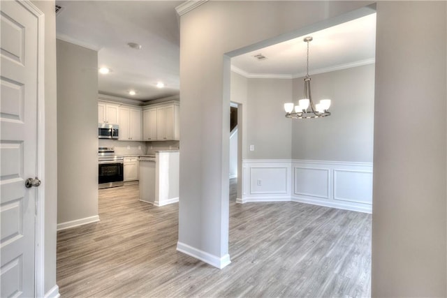 kitchen with white cabinets, crown molding, appliances with stainless steel finishes, decorative light fixtures, and a chandelier