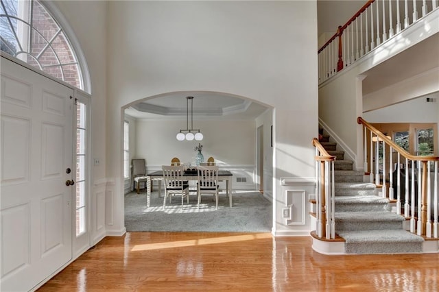 entrance foyer featuring arched walkways, light wood finished floors, a towering ceiling, and crown molding