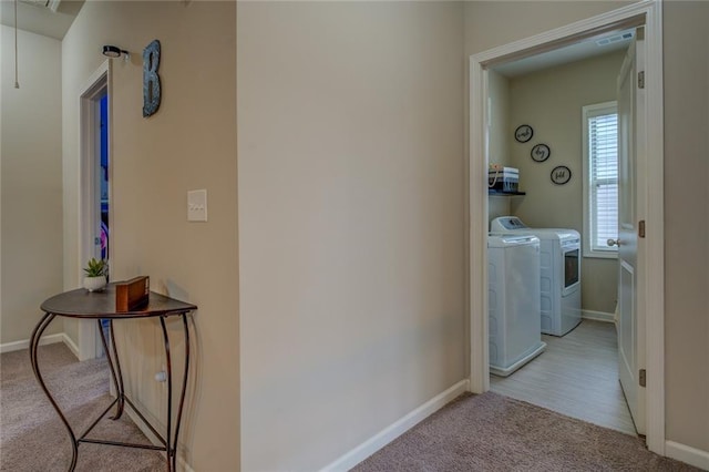 corridor featuring attic access, washing machine and dryer, light colored carpet, and baseboards