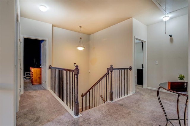 hall featuring attic access, carpet, baseboards, and an upstairs landing