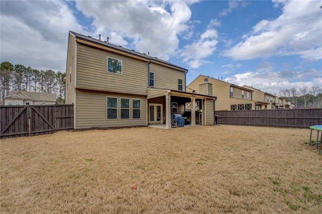 rear view of property with a trampoline, a yard, a patio, a gate, and a fenced backyard