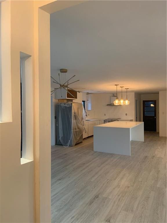 kitchen with white cabinetry, a kitchen island, light wood-type flooring, and decorative light fixtures