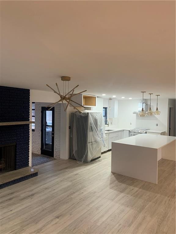 kitchen featuring sink, white cabinetry, a brick fireplace, light hardwood / wood-style flooring, and pendant lighting