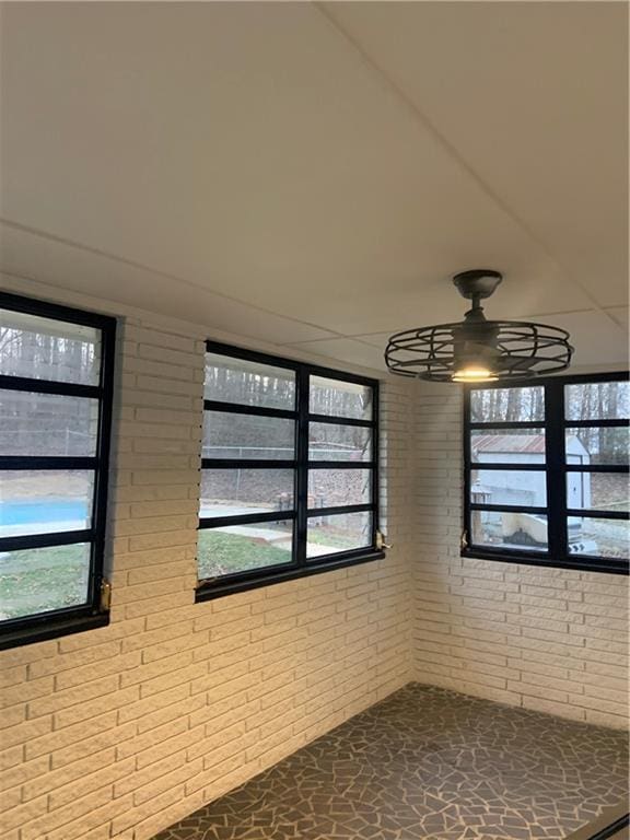 unfurnished room with a wealth of natural light, ceiling fan, and brick wall