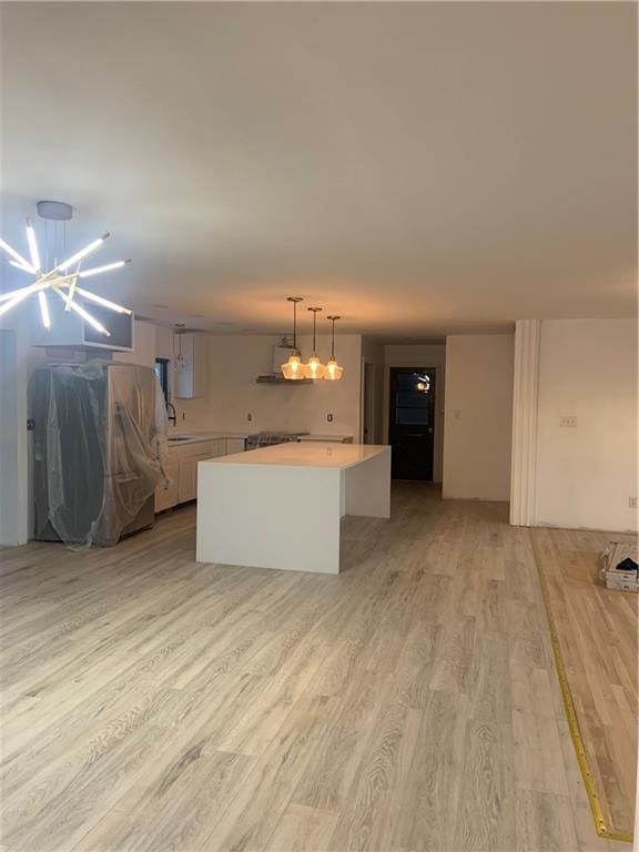 kitchen featuring hanging light fixtures, white cabinets, a kitchen island, a chandelier, and light wood-type flooring