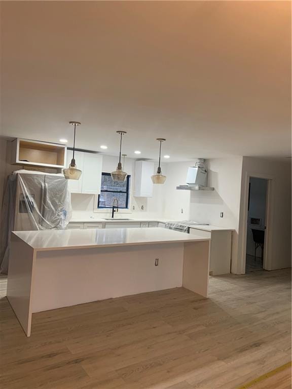 kitchen with wall chimney range hood, sink, light hardwood / wood-style flooring, hanging light fixtures, and white cabinets