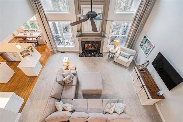 living room with sink, a towering ceiling, ceiling fan, a fireplace, and light hardwood / wood-style floors