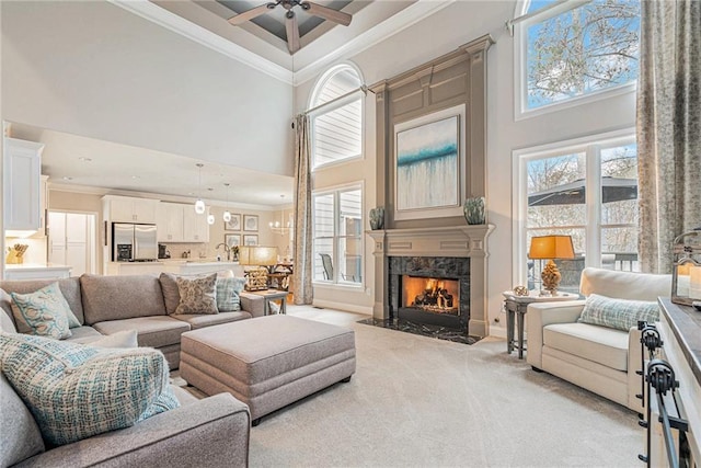 carpeted living room featuring a towering ceiling, a wealth of natural light, ornamental molding, and a premium fireplace