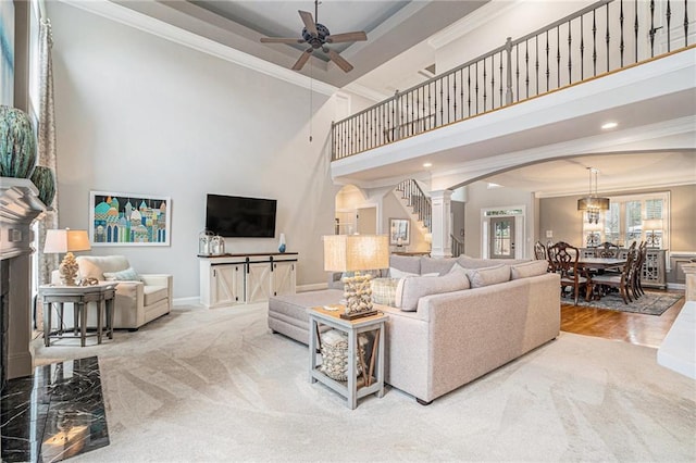 living room with crown molding, ceiling fan, carpet flooring, a towering ceiling, and a high end fireplace