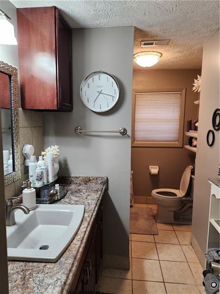 bathroom with tile patterned floors, vanity, toilet, a textured ceiling, and baseboards