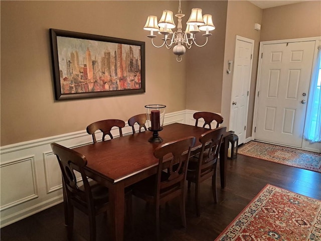 dining space featuring dark wood-type flooring, a decorative wall, wainscoting, and an inviting chandelier