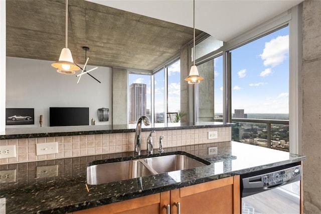 kitchen featuring dishwashing machine, dark stone counters, a sink, brown cabinets, and backsplash