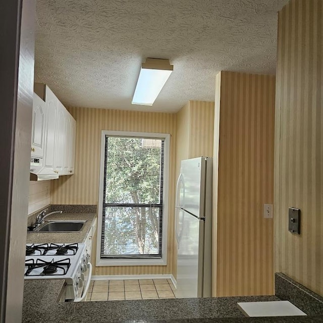 kitchen with dark countertops, white appliances, white cabinetry, and a sink