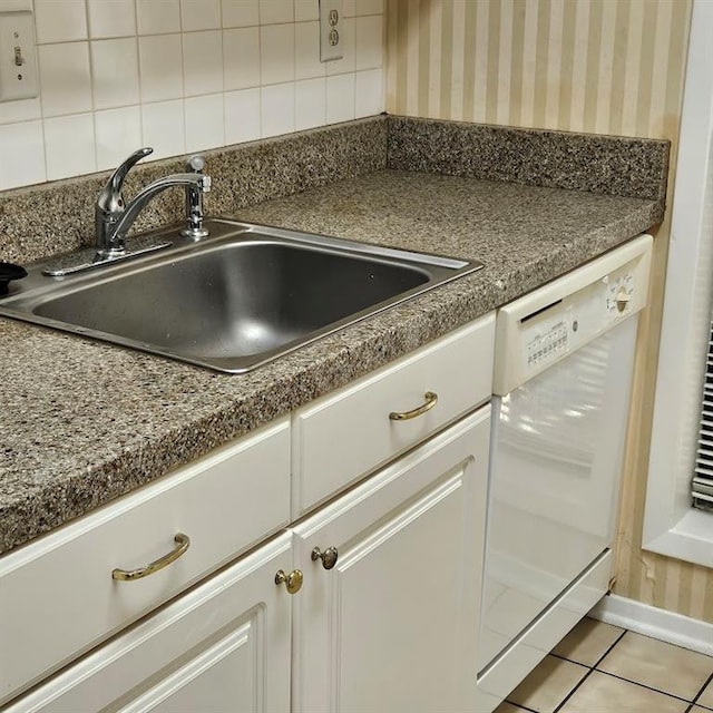 kitchen with light tile patterned floors, white dishwasher, a sink, decorative backsplash, and dark countertops