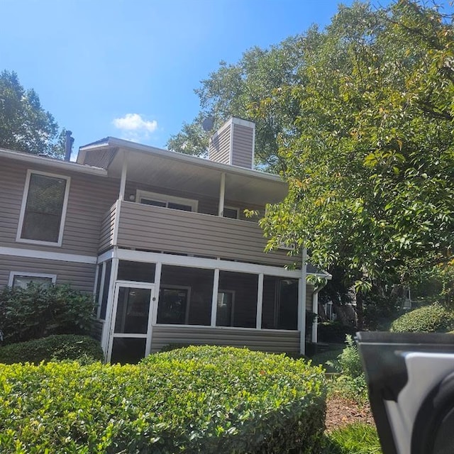 back of property with a balcony, a sunroom, and a chimney